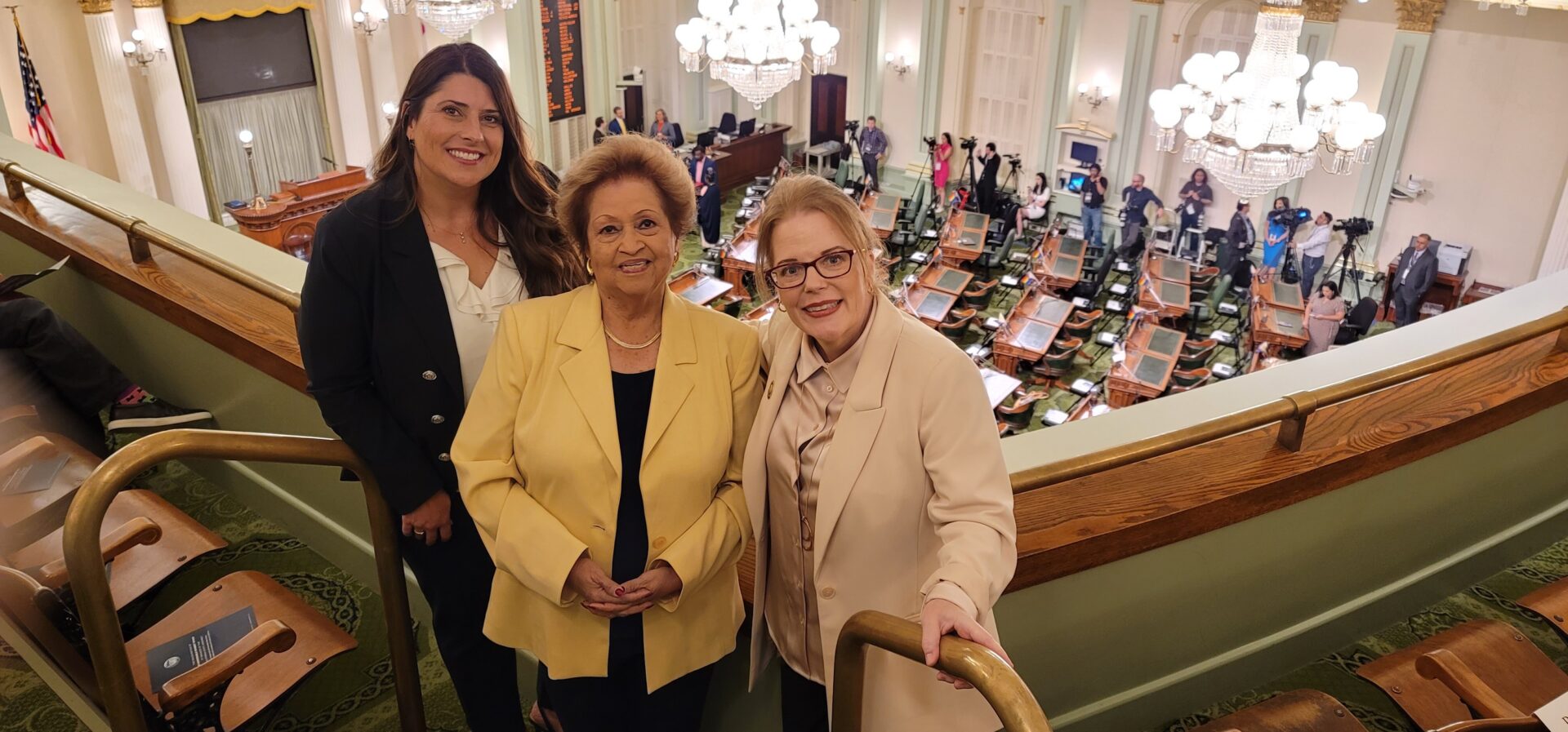 Three women standing in a room with other people.