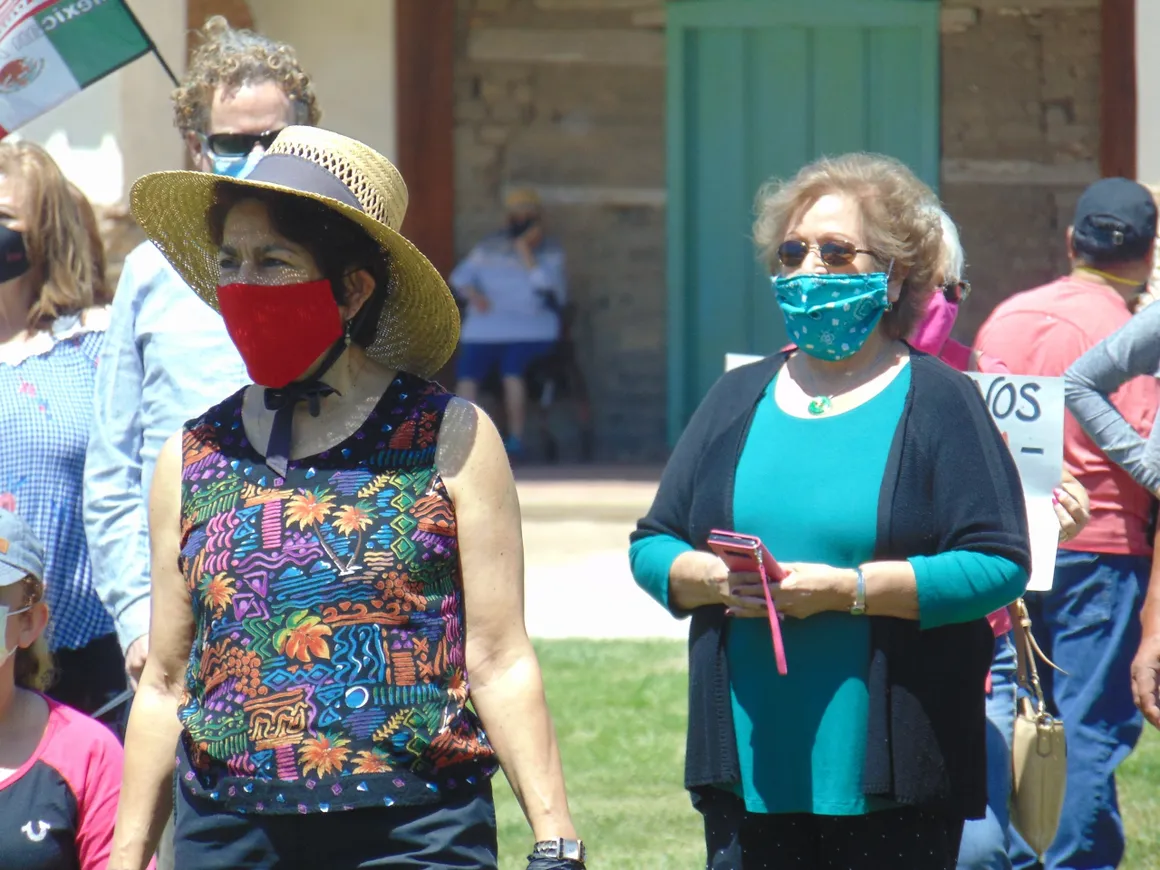 Two women wearing masks and standing in a park.