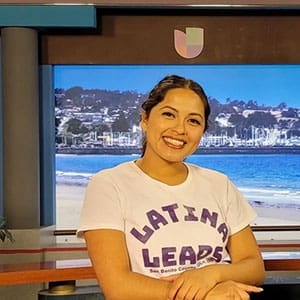 A woman in front of a tv smiling for the camera.